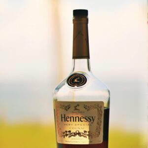 Close-up of a Hennessy cognac bottle with a blurred outdoor background, showcasing its elegance.