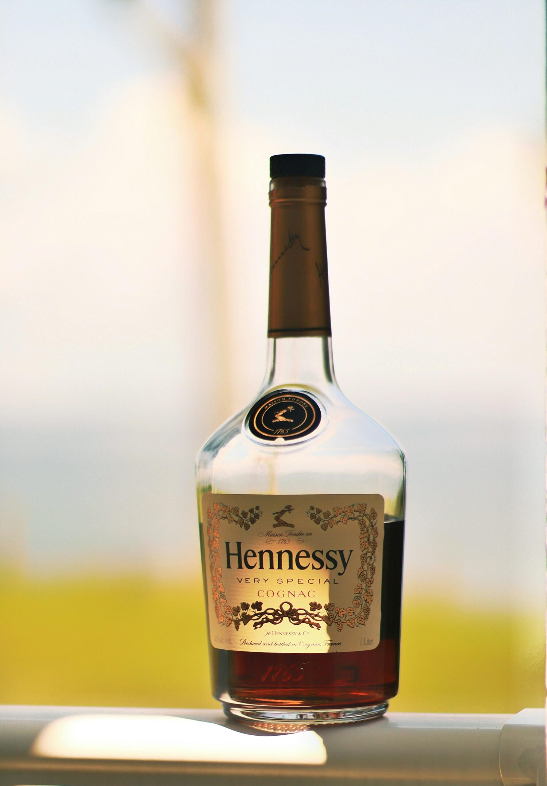 pexels photo 13463111 13463111 Close-up of a Hennessy cognac bottle with a blurred outdoor background, showcasing its elegance.